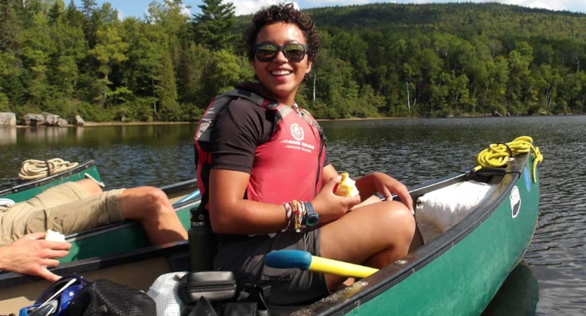 A person sitting in a canoe wearing a lifejacket smiles at the camera